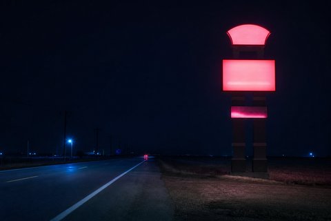 A tall illuminated casino pylon sign beside an empty two-lane highway at night, with flat open country either side.