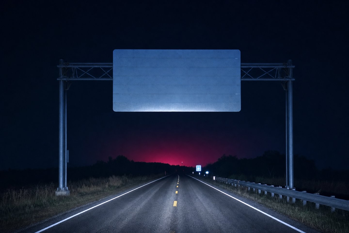 A blank retroreflective sign gantry spanning a dark two-lane highway, caught in headlights, with a faint red glow rising from below the horizon beyond it.
