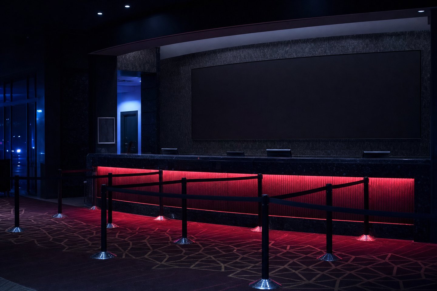 An empty service desk inside a casino at night, a long dark stone counter lit crimson from a recess along its front, a coiled queue barrier of posts and belts in front of it and a blank unlit panel above it.